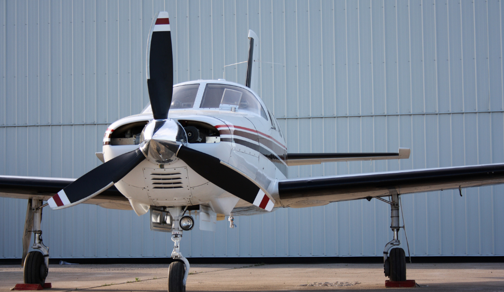 Front view of a training aircraft used for earning a private pilot license, parked near a hangar.